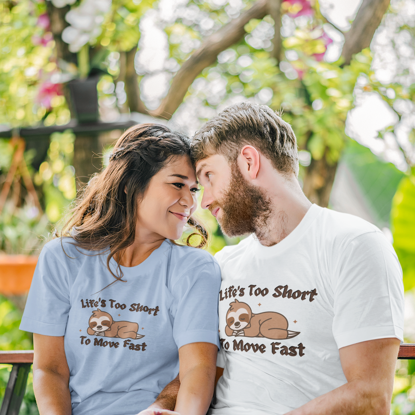Shown is a couple wearing our unisex "Life's Too Short to Move Fast" funny t-shirt, featuring an adorable sleeping sloth graphic on a short sleeve Tee, one in white and the other in Baby Blue.