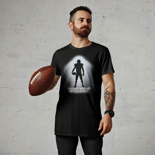 The t-shirt design features a captivating silhouette of a football player standing confidently under a bright spotlight, capturing the essence of the intense anticipation and excitement of draft night. The player's stance exudes determination and readiness, symbolizing the pivotal moment of being in the spotlight as they await their fate in the draft.