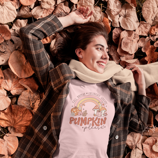 Shown is is a woman wearing our "Fall Breeze, Crunchy Leaves, Pumpkin Please" Women's T-Shirt! This delightful design features a distressed retro-style graphic of a rainbow adorned with pumpkins and mushrooms in fall colors on a short sleeve pink T-shirt.